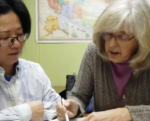 Placeholder image: a tutor pointing to a workbook beside a student.