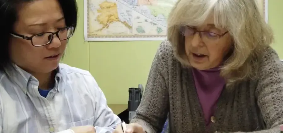 Placeholder image: a tutor pointing to a workbook beside a student.